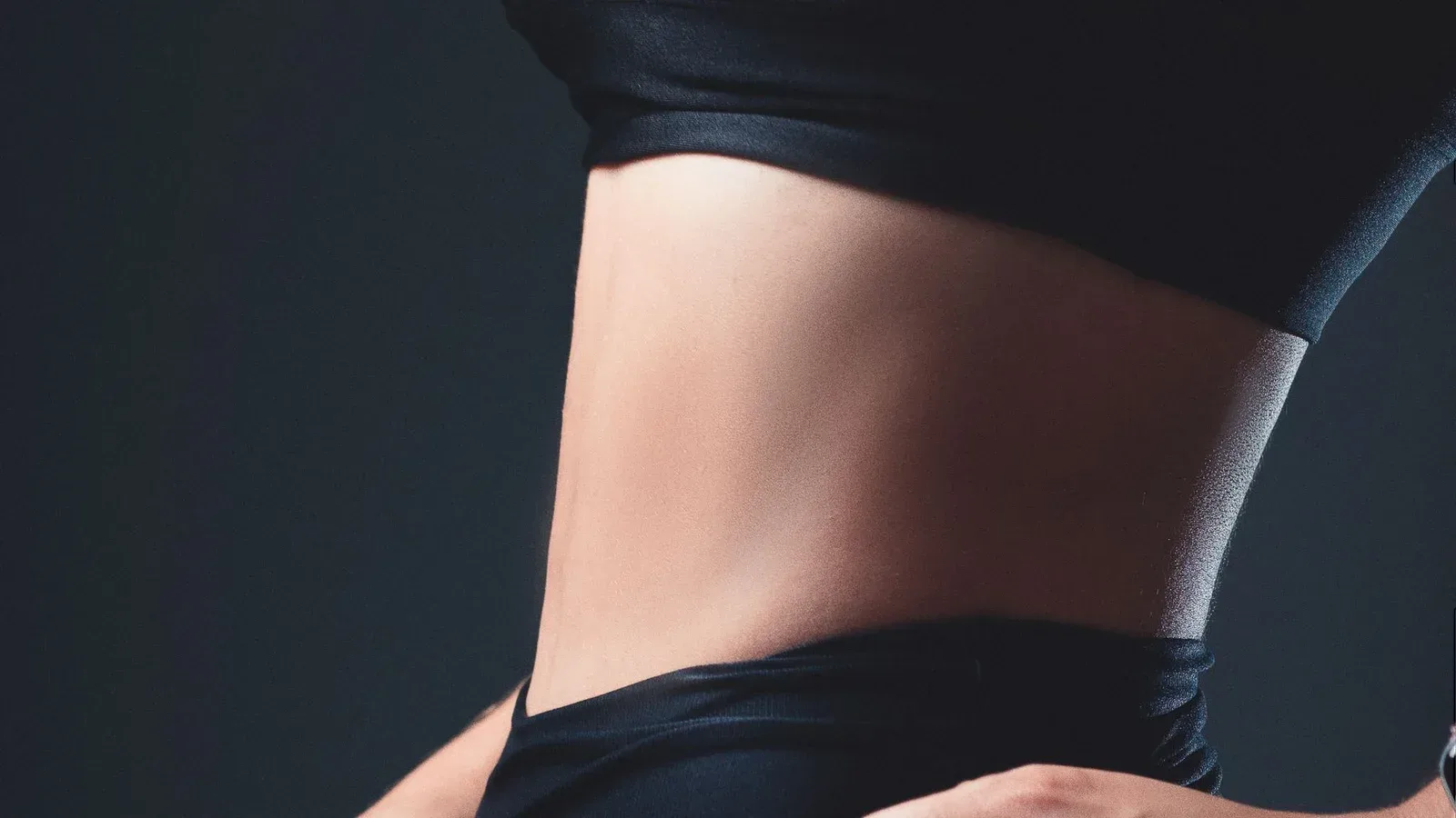 Detalhe de cintura e abdômen feminino com roupa esportiva escura — imagem ilustrativa.